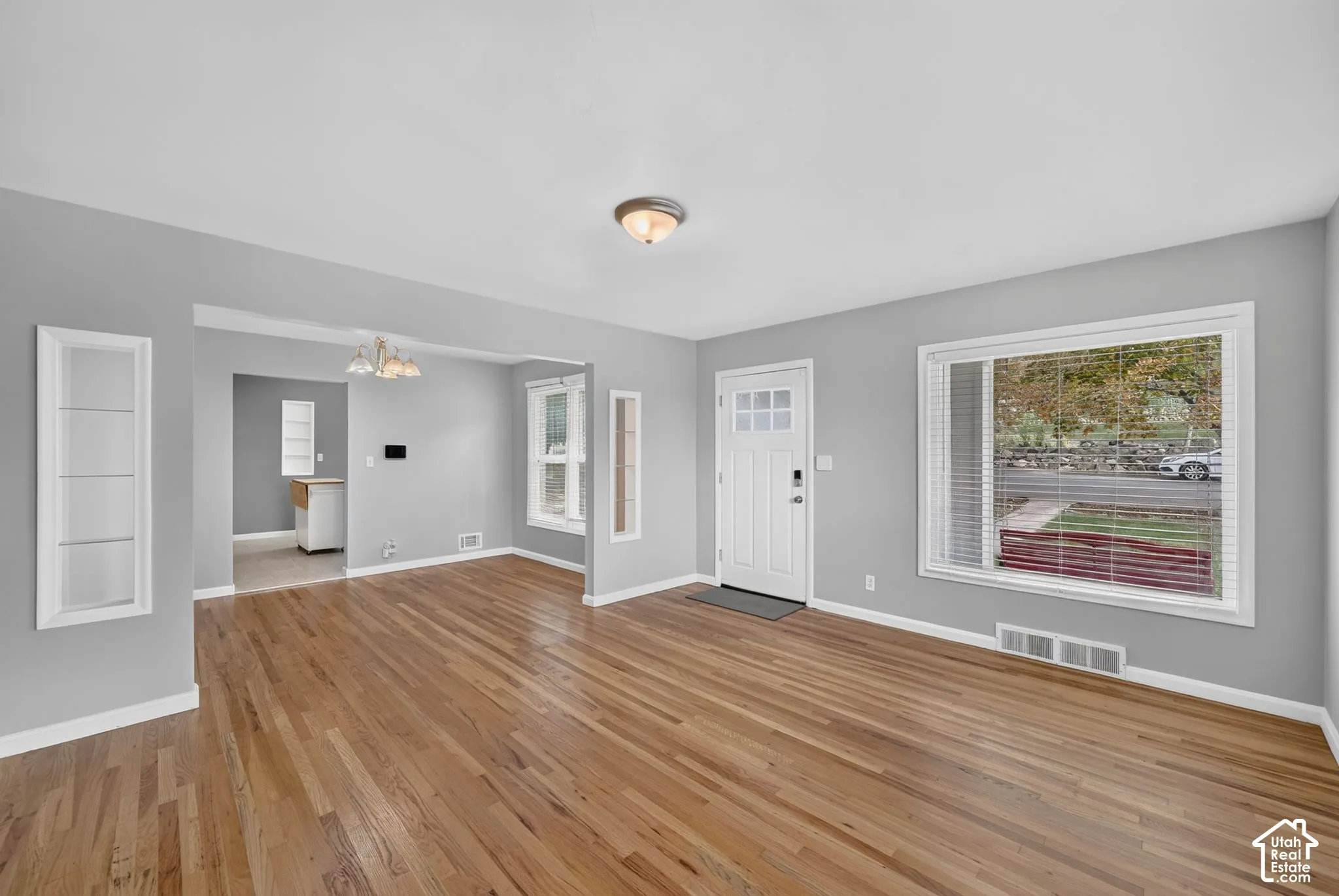 Wood-finish flooring throughout, with a white paneled entry door and a large window featuring horizontal blinds