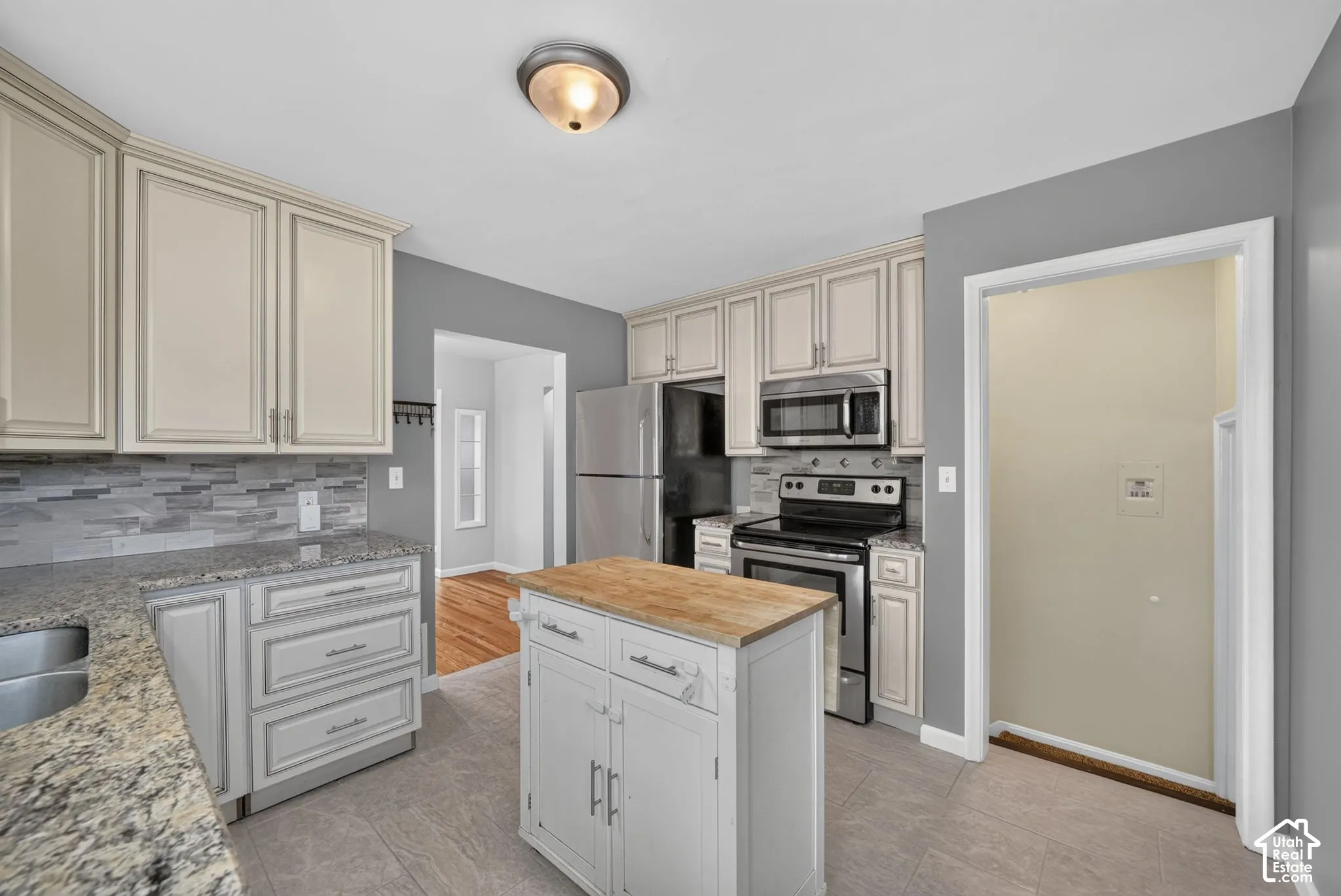 Kitchen featuring light-toned cabinetry, granite countertops, tile flooring, and stainless steel appliances