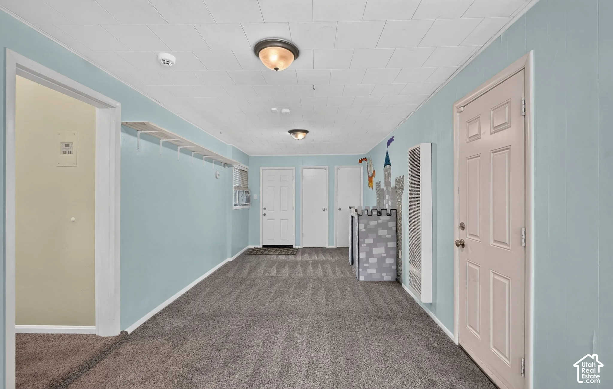 Recessed panel doors, wall-mounted air conditioning unit, ceiling-mounted light fixtures, textured ceiling, and gray carpet flooring