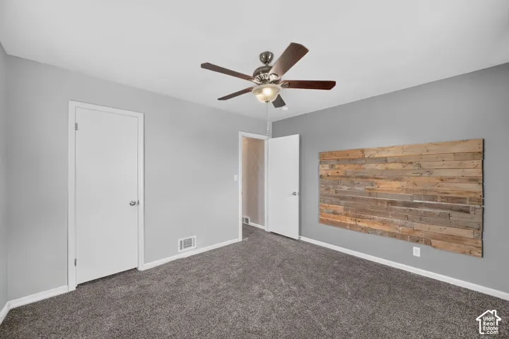 Wall-mounted wood paneling detail, textured carpet flooring, two interior doors, and a ceiling fan with integrated lighting
