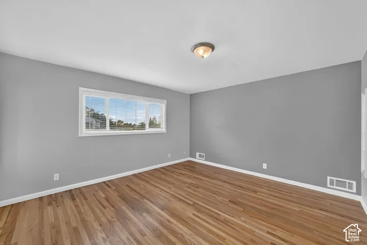 Hardwood flooring, neutral gray wall tones, ceiling-mounted light fixture, white window trim, and white baseboards