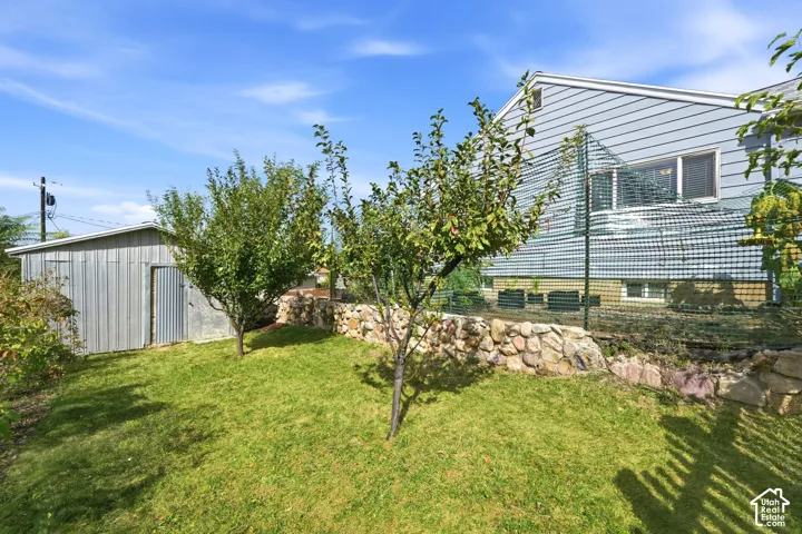 Expansive yard featuring a corrugated metal shed, stone retaining wall, and mature trees