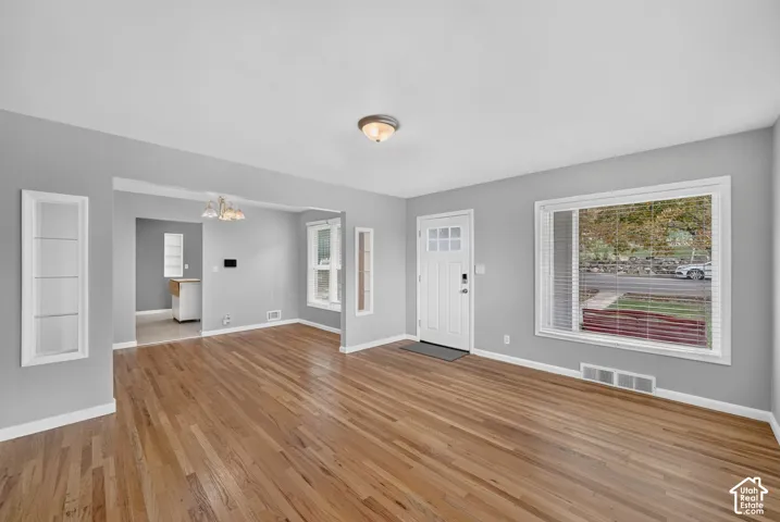 Wood-finish flooring throughout, with a white paneled entry door and a large window featuring horizontal blinds