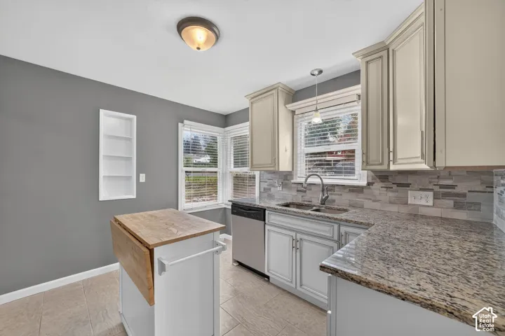 Cream cabinetry with brushed nickel hardware, granite countertops, tile backsplash, stainless steel sink with gooseneck faucet, and tile flooring