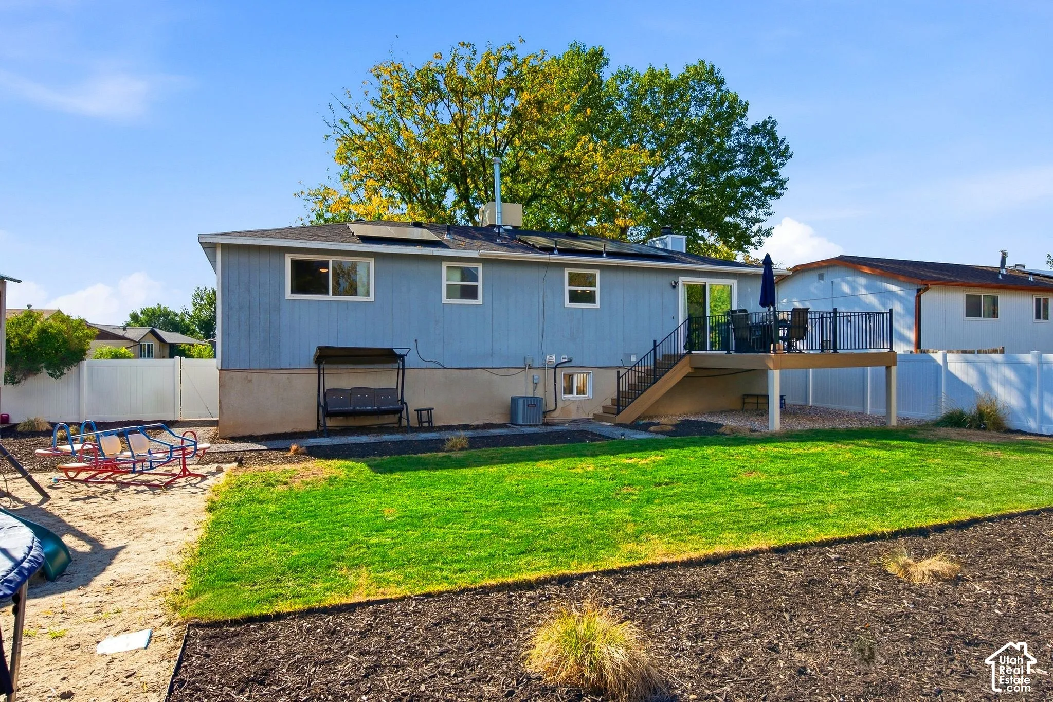 Exterior featuring a raised deck with black railings, a sliding glass door, a gravel area beneath the deck, and solar panels on the roof