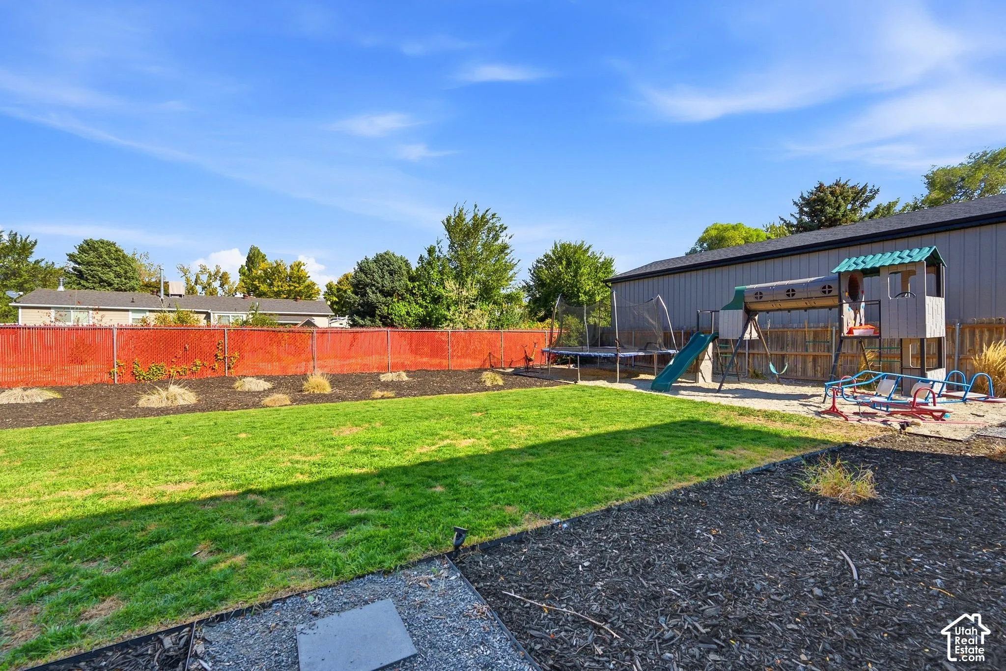 Expansive backyard featuring a manicured lawn, red privacy fence, and a spacious outbuilding