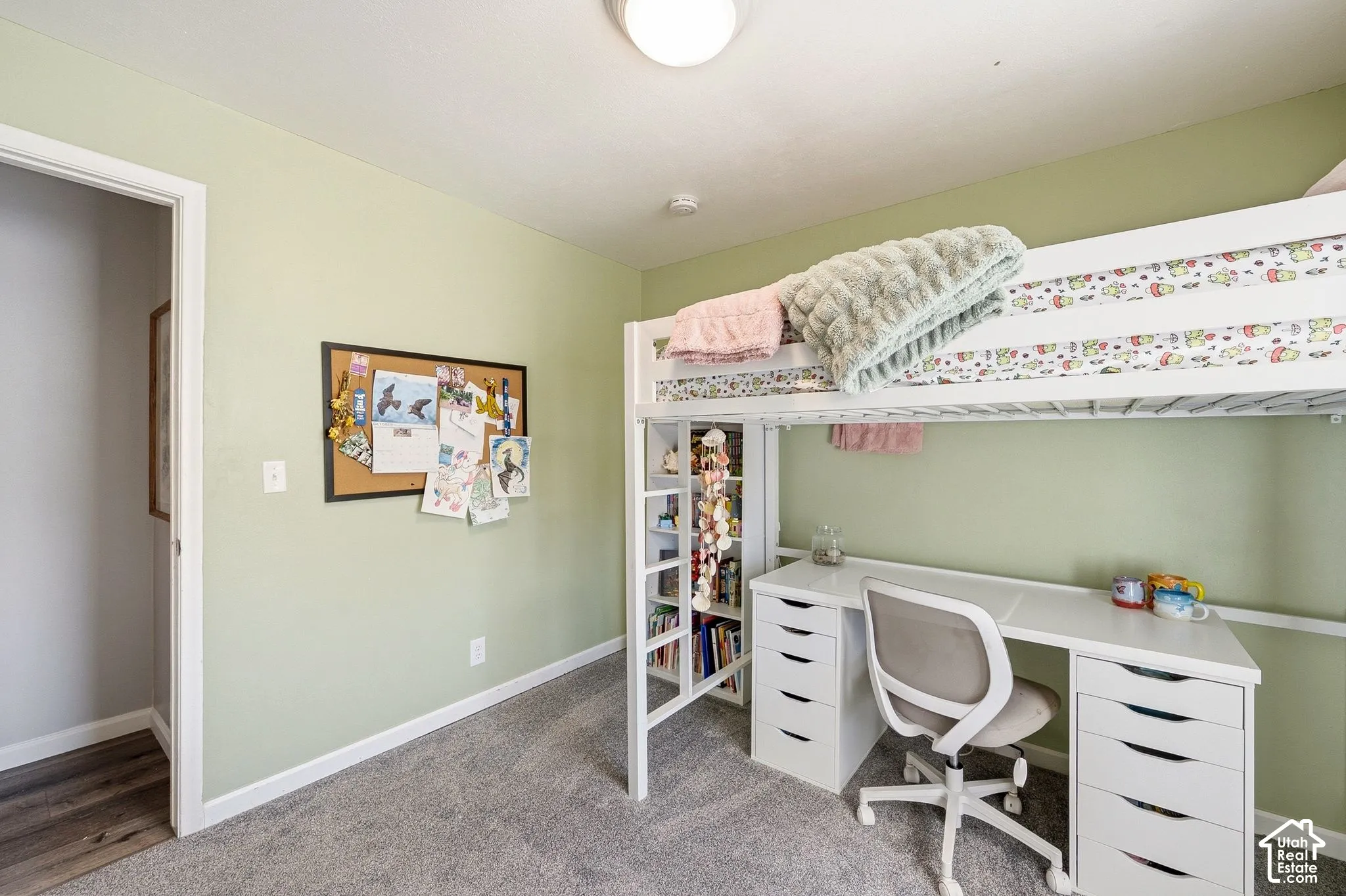 Carpeted flooring, light green painted walls, white trim, and a white built-in desk with multiple drawers