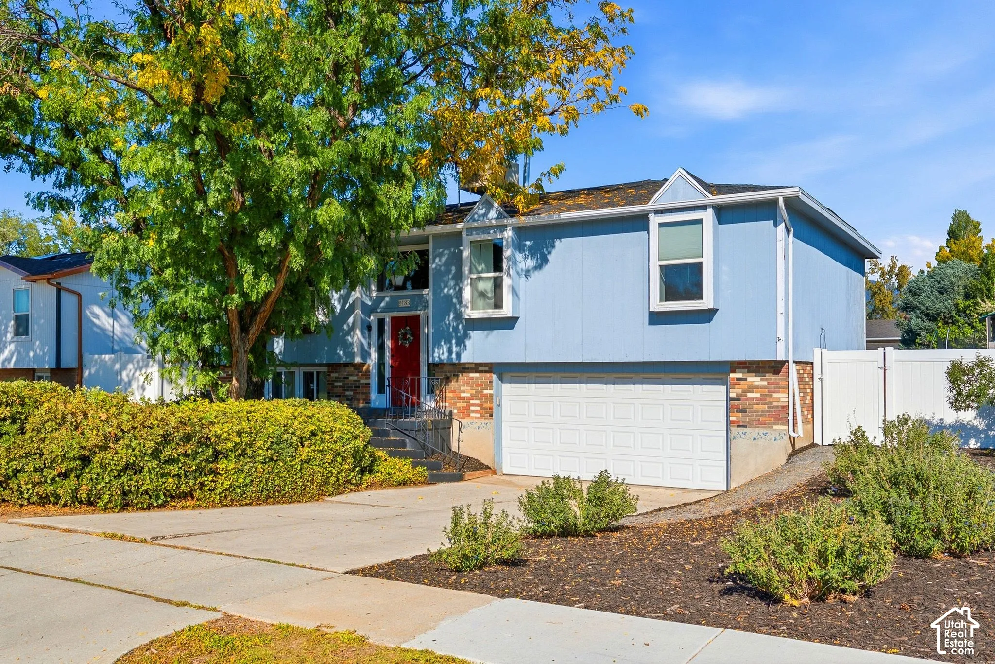 Split-level residence featuring blue siding, a red entry door, an attached two-car garage, and a concrete driveway