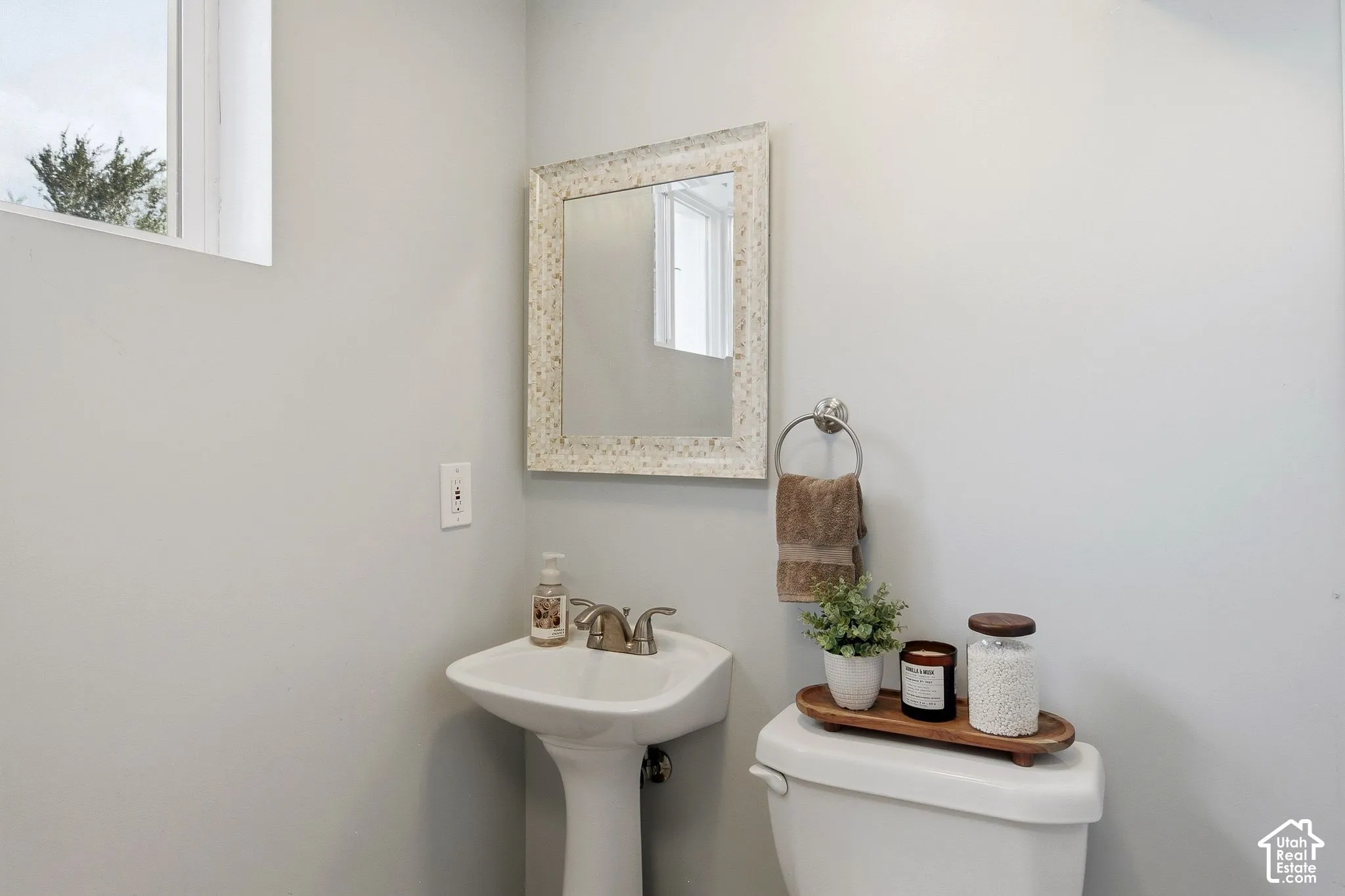 Pedestal sink with chrome-finish faucet, mirror with textured frame, and a window for natural light