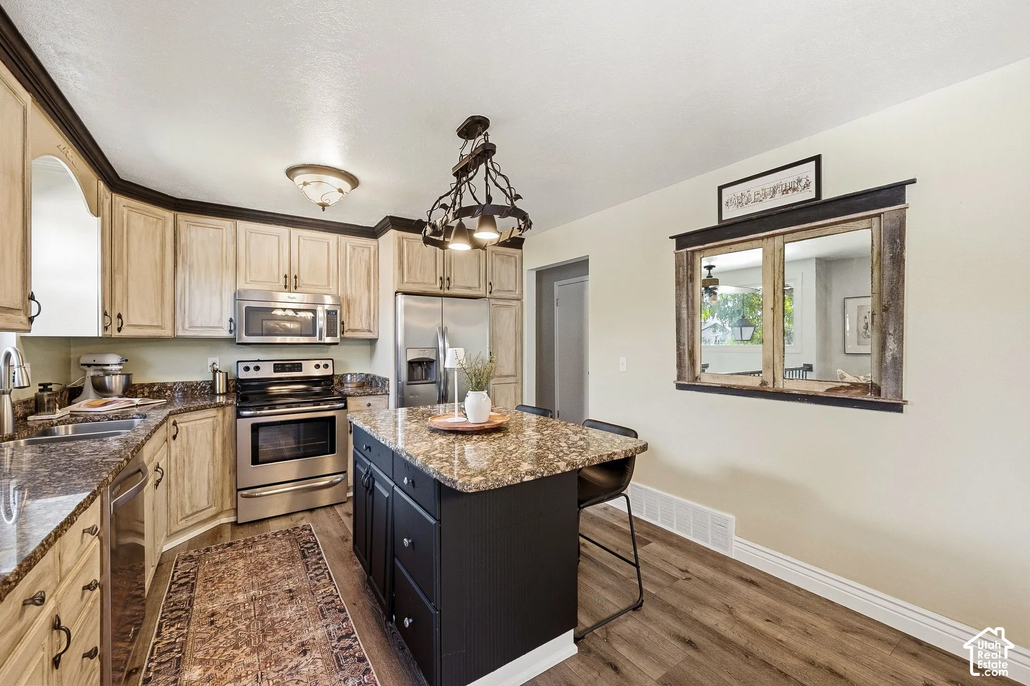 Kitchen featuring wood-finish flooring, an island with stone-finish countertop, stainless steel appliances, and wood cabinetry with dark trim