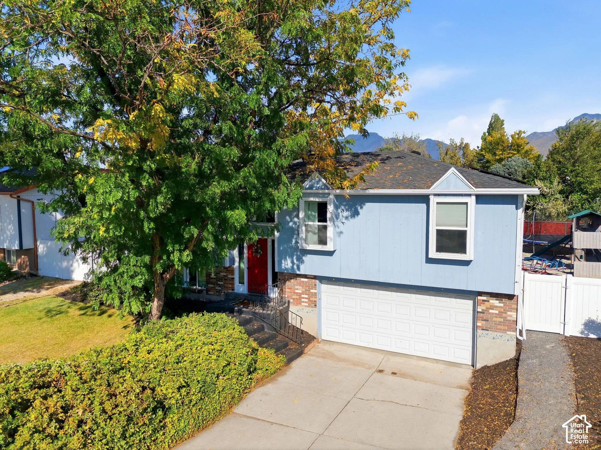 Split-level residence featuring light blue siding with brick accents and a prominent red entry door