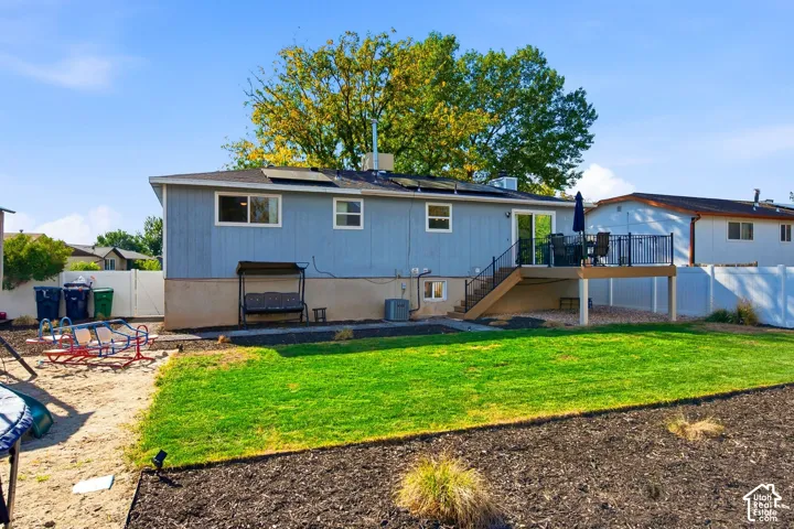 Expansive green lawn, elevated deck with railing, sliding glass door access, solar panels on roof, and additional lower-level window