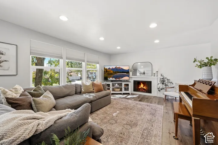 Living area featuring wood-finish flooring, recessed lighting, and large windows with privacy blinds