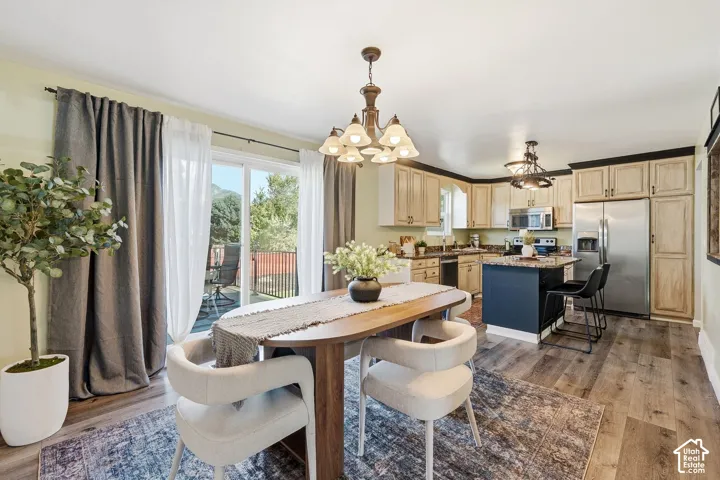 Open-concept dining and kitchen space with wood-finish flooring, a kitchen island with seating, stainless steel appliances, and sliding glass doors to an outdoor deck