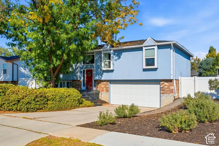 Split-level residence featuring blue siding, a red entry door, an attached two-car garage, and a concrete driveway
