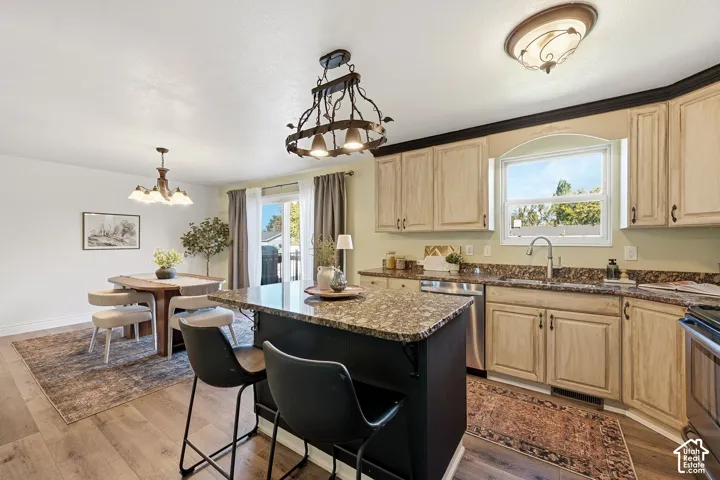 Kitchen featuring a center island with granite countertop, light wood-finish cabinetry, stainless steel dishwasher, and a window above the sink
