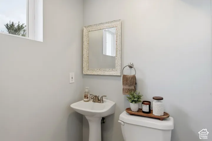 Pedestal sink with chrome-finish faucet, mirror with textured frame, and a window for natural light