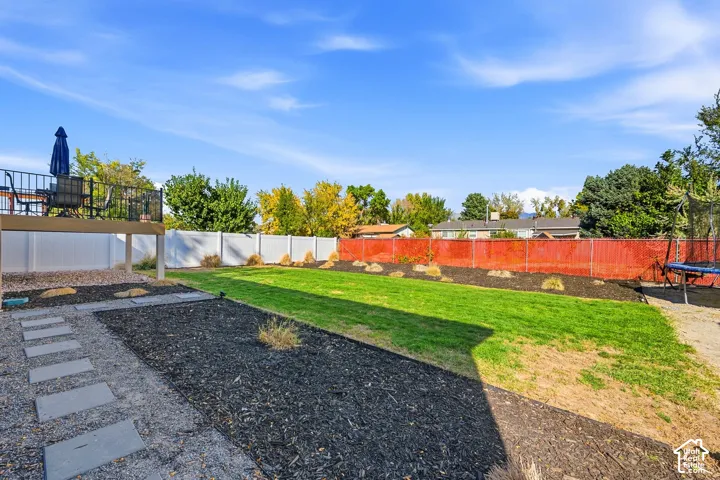 Expansive backyard featuring a manicured lawn, an elevated deck with black railing, a white privacy fence, and a gravel pathway with stepping stones