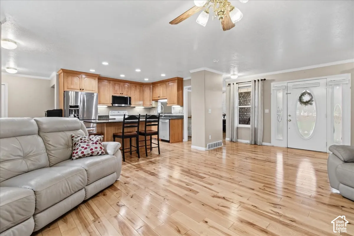 Open-concept living area featuring wood-finish flooring, a kitchen with wood cabinetry, stainless steel appliances, and a black countertop, and a white entry door with frosted glass panels