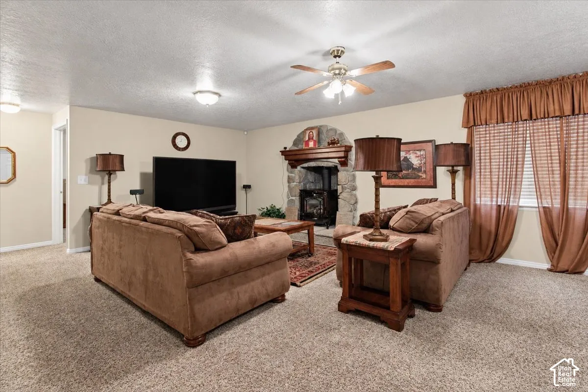 Stone fireplace with wood mantel, ceiling fan, recessed lighting, and carpeted flooring