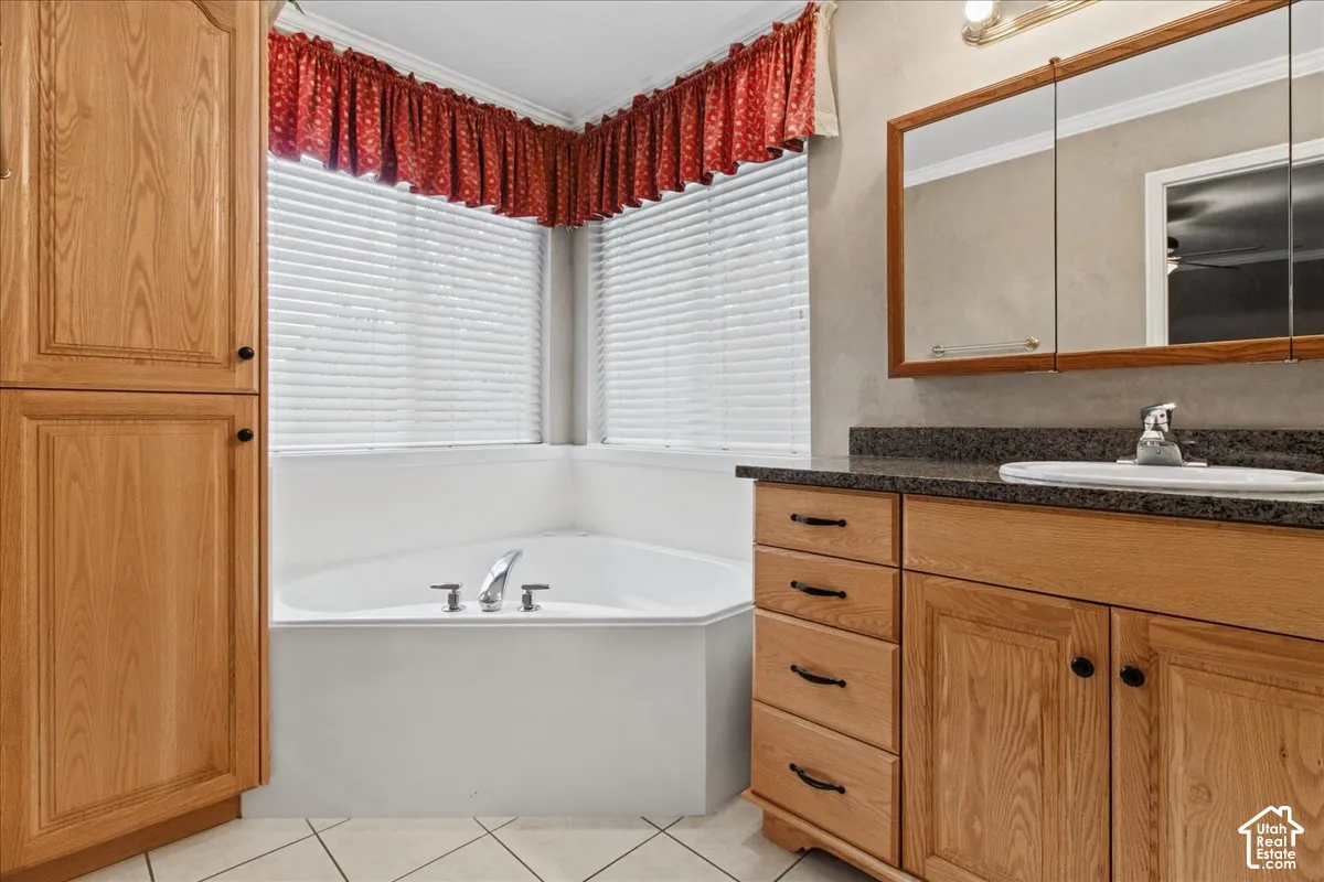 Corner bathtub with chrome fixtures, wood-finish cabinetry, dark countertop with integrated sink, and a mirrored medicine cabinet