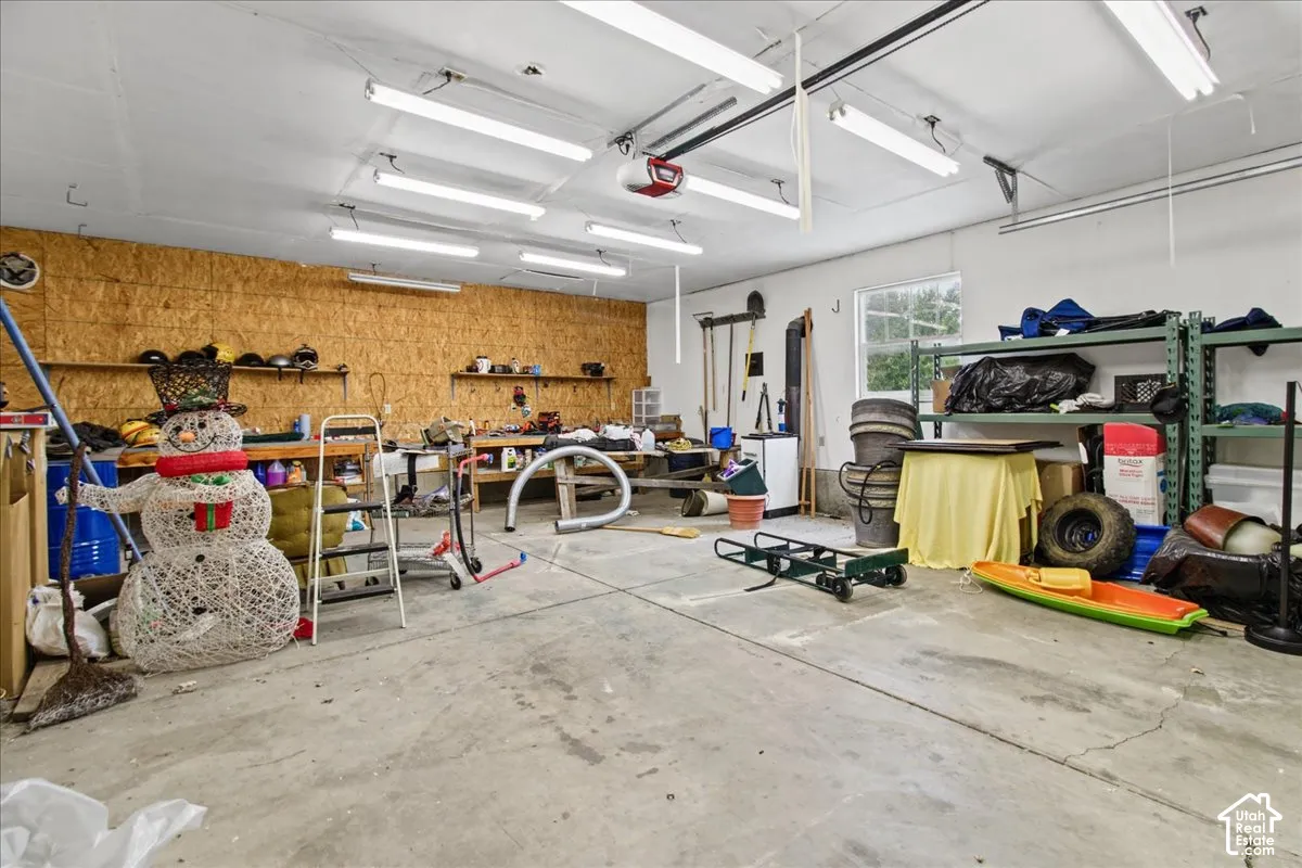 Concrete floor, exposed wood paneling, multiple fluorescent light fixtures, overhead garage door mechanism, single window