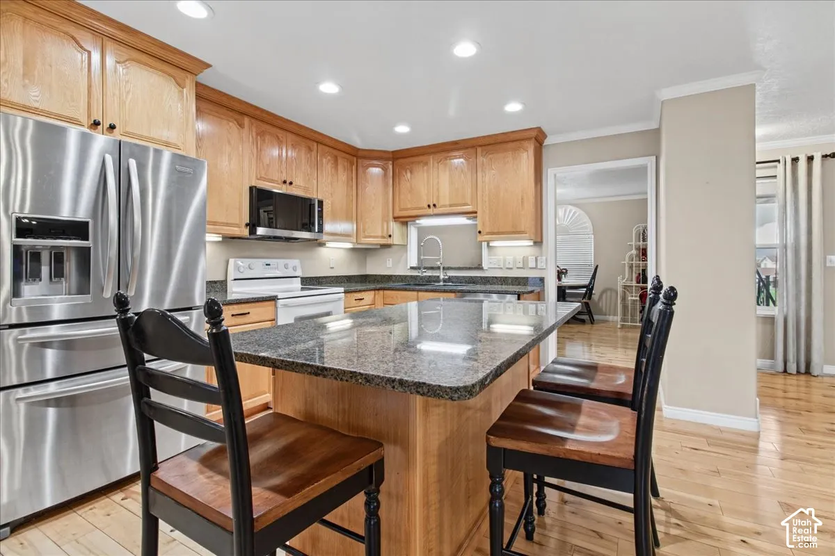 Kitchen featuring wood-finish cabinetry, stainless steel appliances, a center island with a stone countertop, recessed lighting, and wood-finish flooring