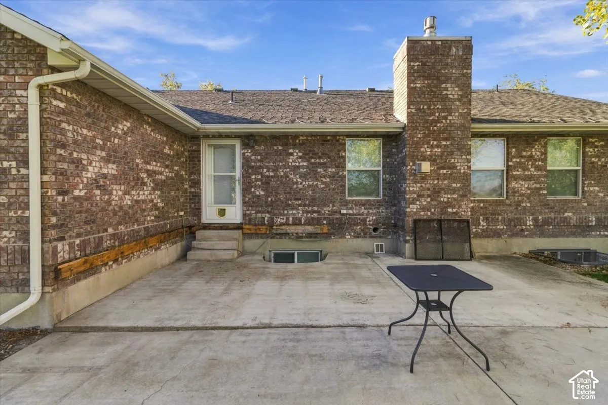 Brick exterior with concrete patio, multiple windows, and a prominent brick chimney