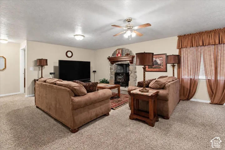 Stone fireplace with wood mantel, ceiling fan, recessed lighting, and carpeted flooring