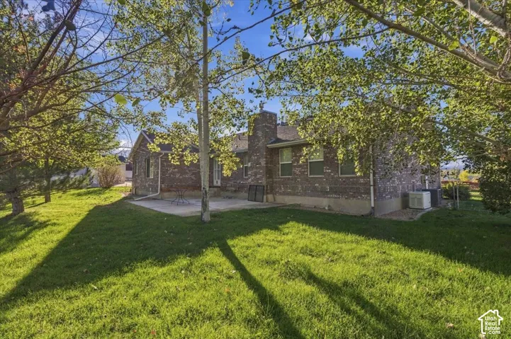 Expansive green lawn with mature trees, a brick-clad exterior, and a spacious concrete patio