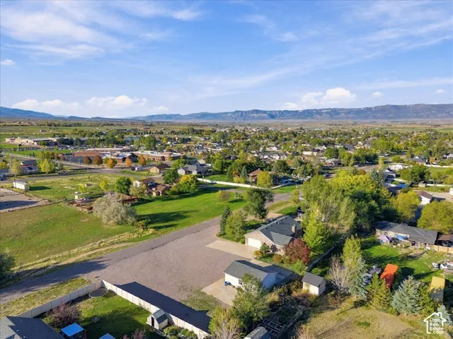 Aerial perspective showcasing expansive grounds with mature landscaping, multiple outbuildings, established trees throughout the property, and pastoral mountain backdrop with distant ridgeline