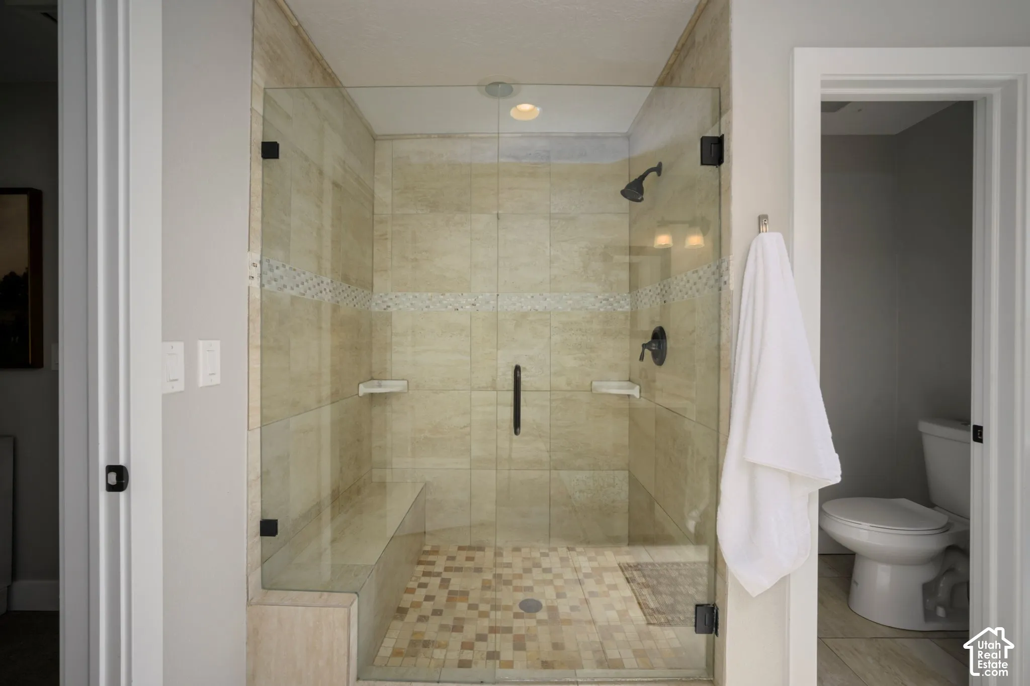 Glass-enclosed shower with a built-in bench, tiled walls, and a mosaic tile floor
