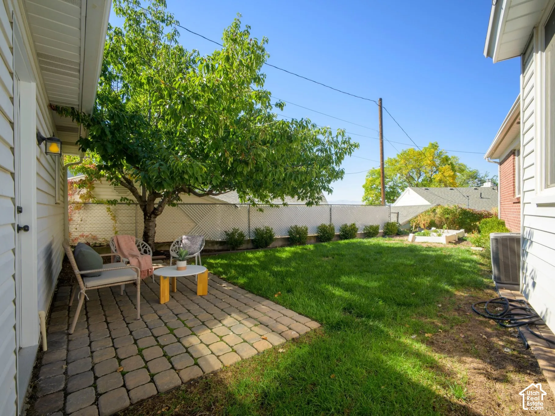 Paved patio area, mature tree, manicured lawn, white lattice fencing, and a raised garden bed