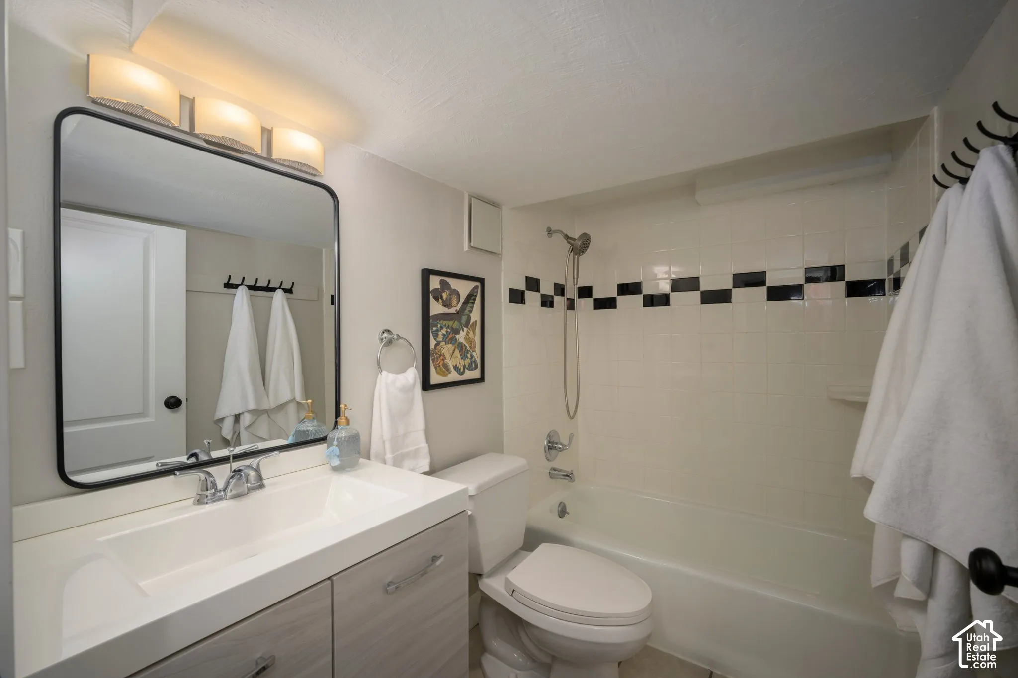 Bathroom featuring a vanity with an integrated sink, a large framed mirror, a three-light fixture, a toilet, and a bathtub with tiled surround