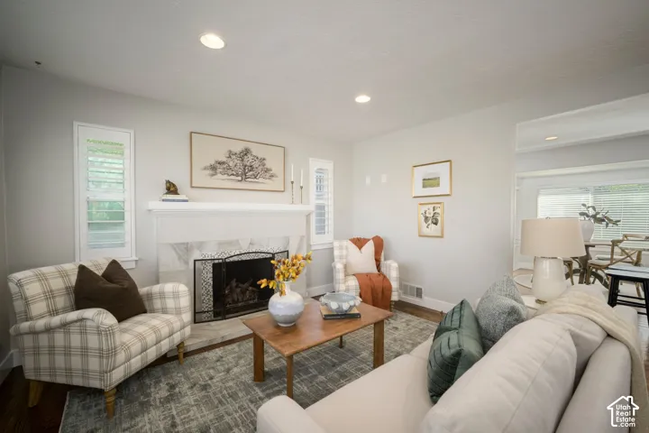 Recessed lighting, hardwood flooring, fireplace with stone surround, white plantation shutters, and a large wall opening to an adjacent room