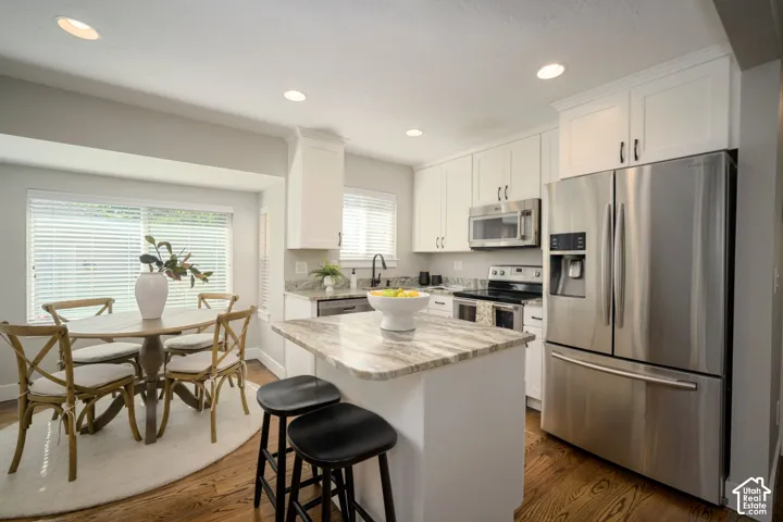 Kitchen featuring white cabinetry, stainless steel appliances, a center island with a granite countertop, recessed lighting, hardwood flooring and dining area.