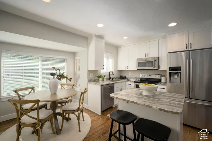 Kitchen featuring white cabinetry, stainless steel appliances, granite countertops and hardwood flooring.