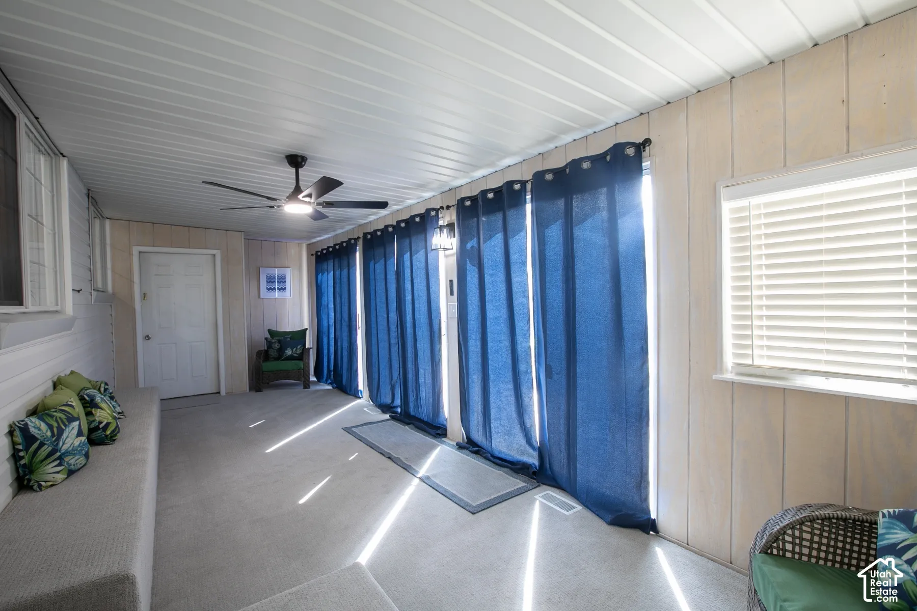 Enclosed patio featuring a ceiling fan, white paneled walls, and a window with blinds