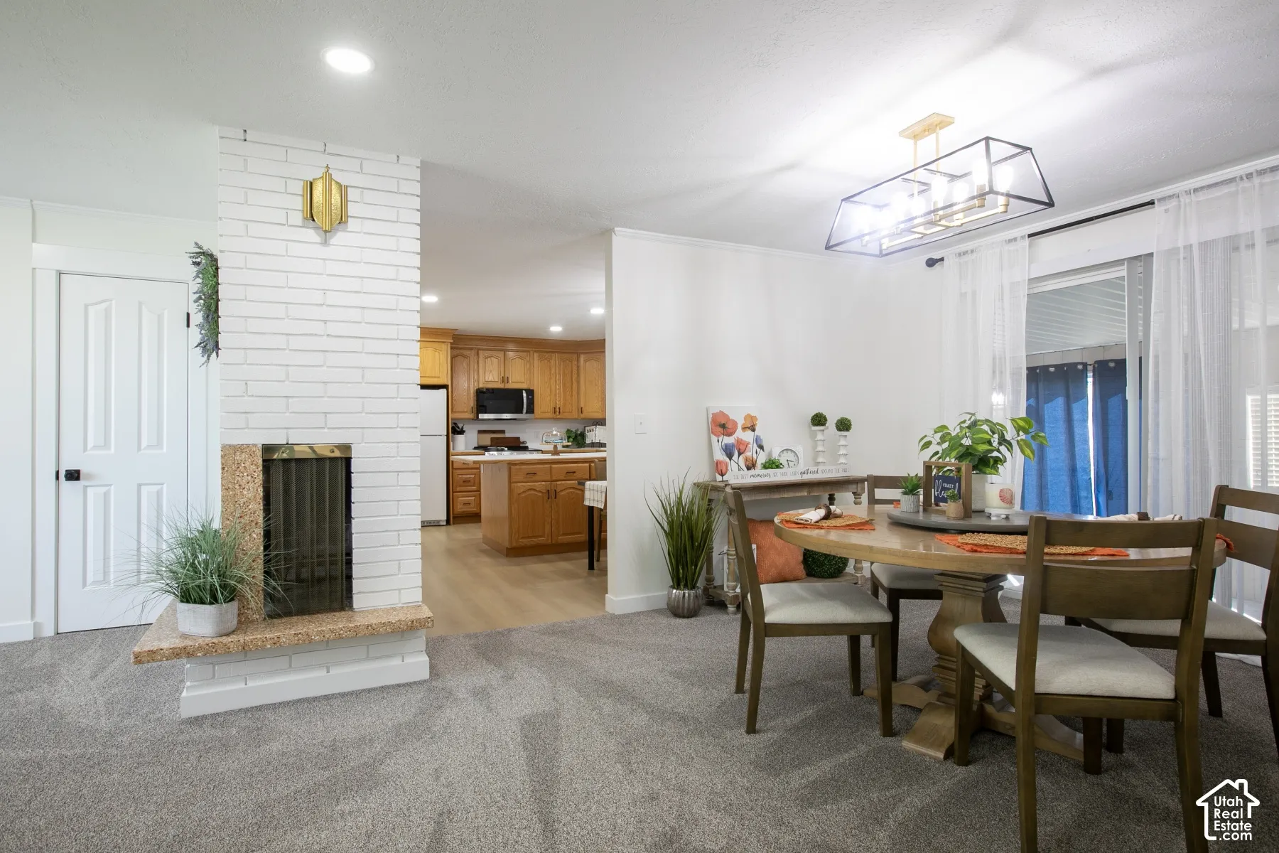 White brick fireplace with a granite hearth, light gray carpeting, and a modern rectangular chandelier