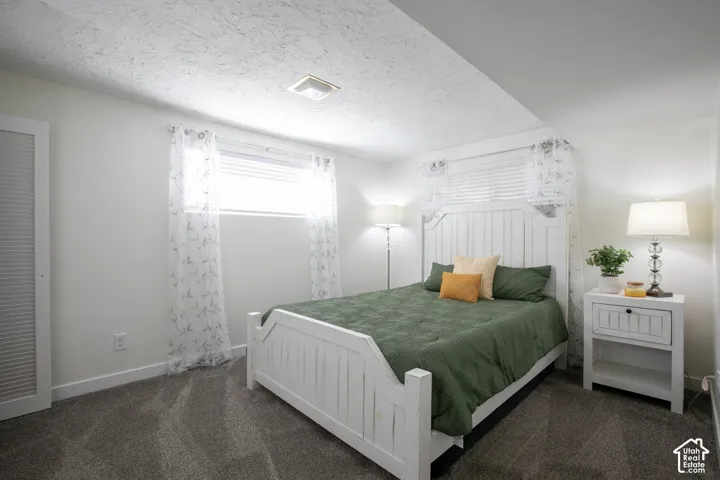 White textured ceiling, gray carpet flooring, window with blinds, and a white paneled bed frame