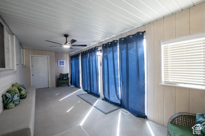 Enclosed patio featuring a ceiling fan, white paneled walls, and a window with blinds