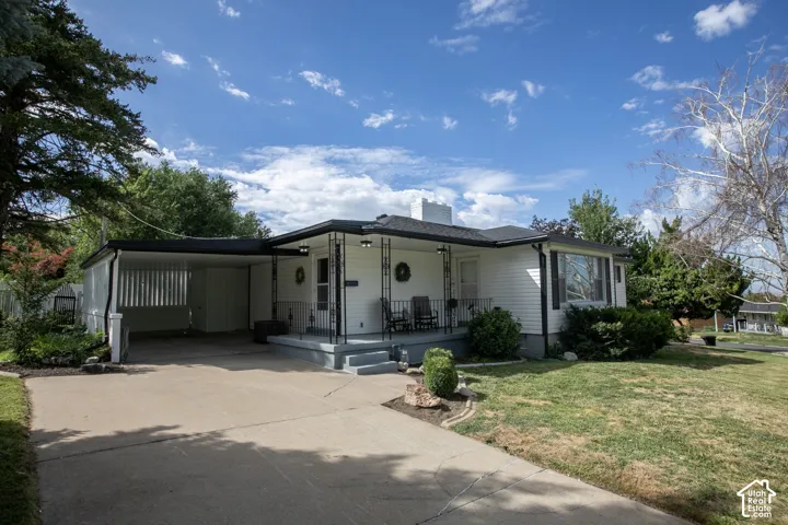 White siding exterior with a dark roof, covered front porch, and an attached carport