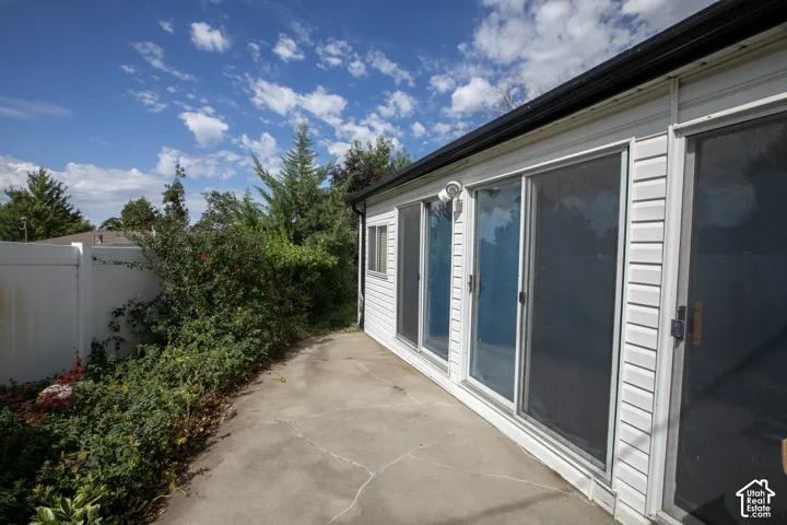 Rear exterior with white siding, multiple sliding glass doors, concrete patio, and mature landscaping