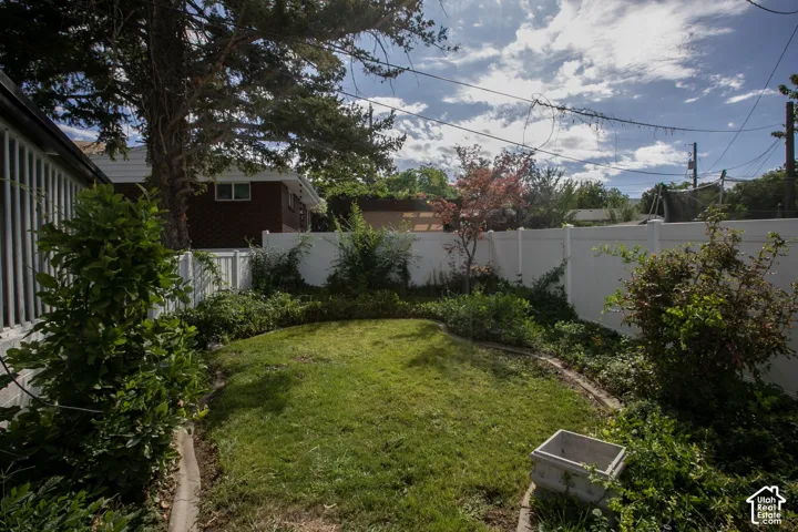 Manicured lawn framed by mature trees and shrubs, featuring a white privacy fence