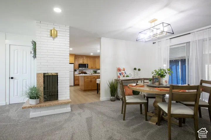White brick fireplace with a granite hearth, light gray carpeting, and a modern rectangular chandelier