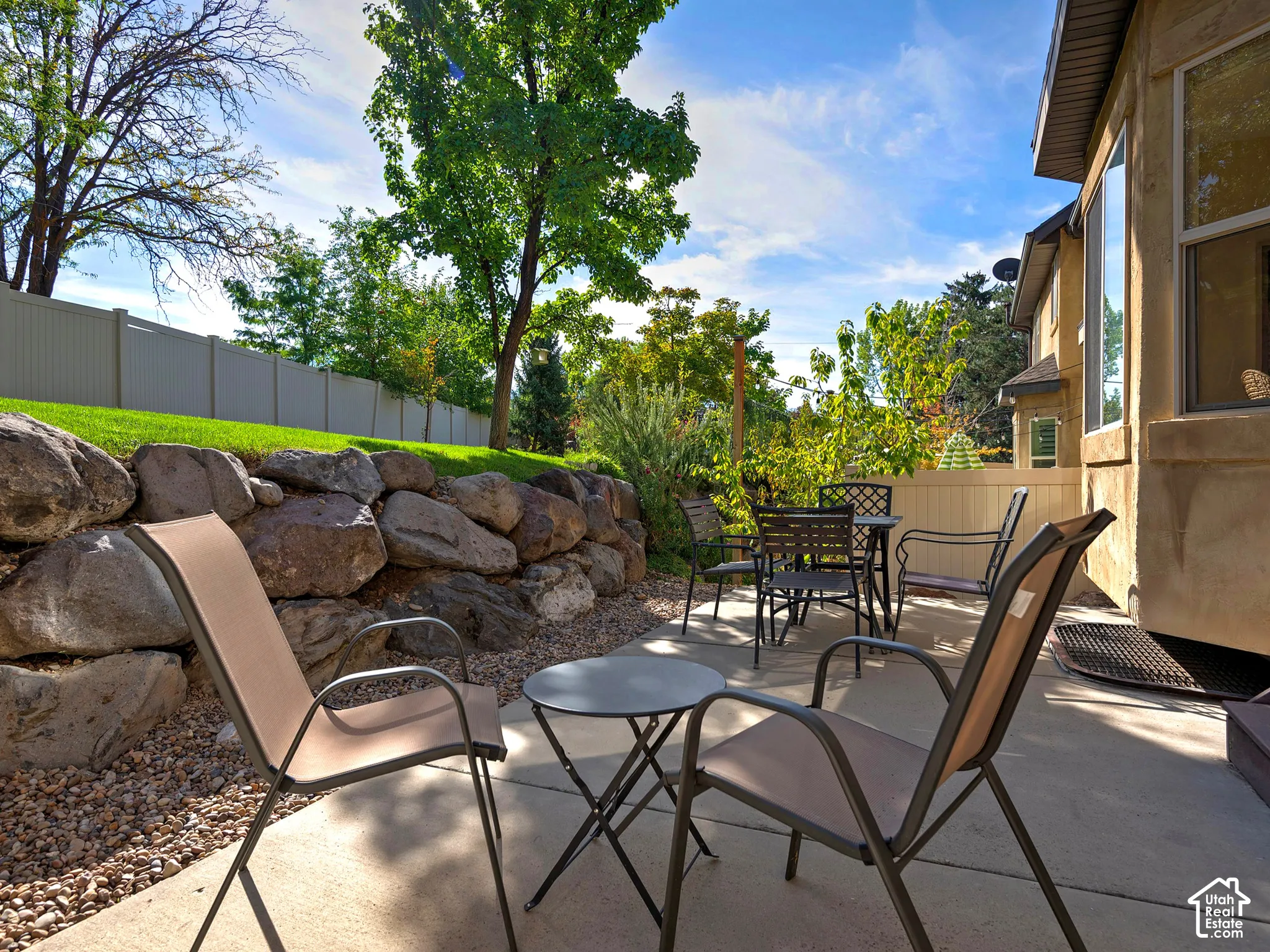 Concrete patio with a rock retaining wall, mature trees, and a privacy fence