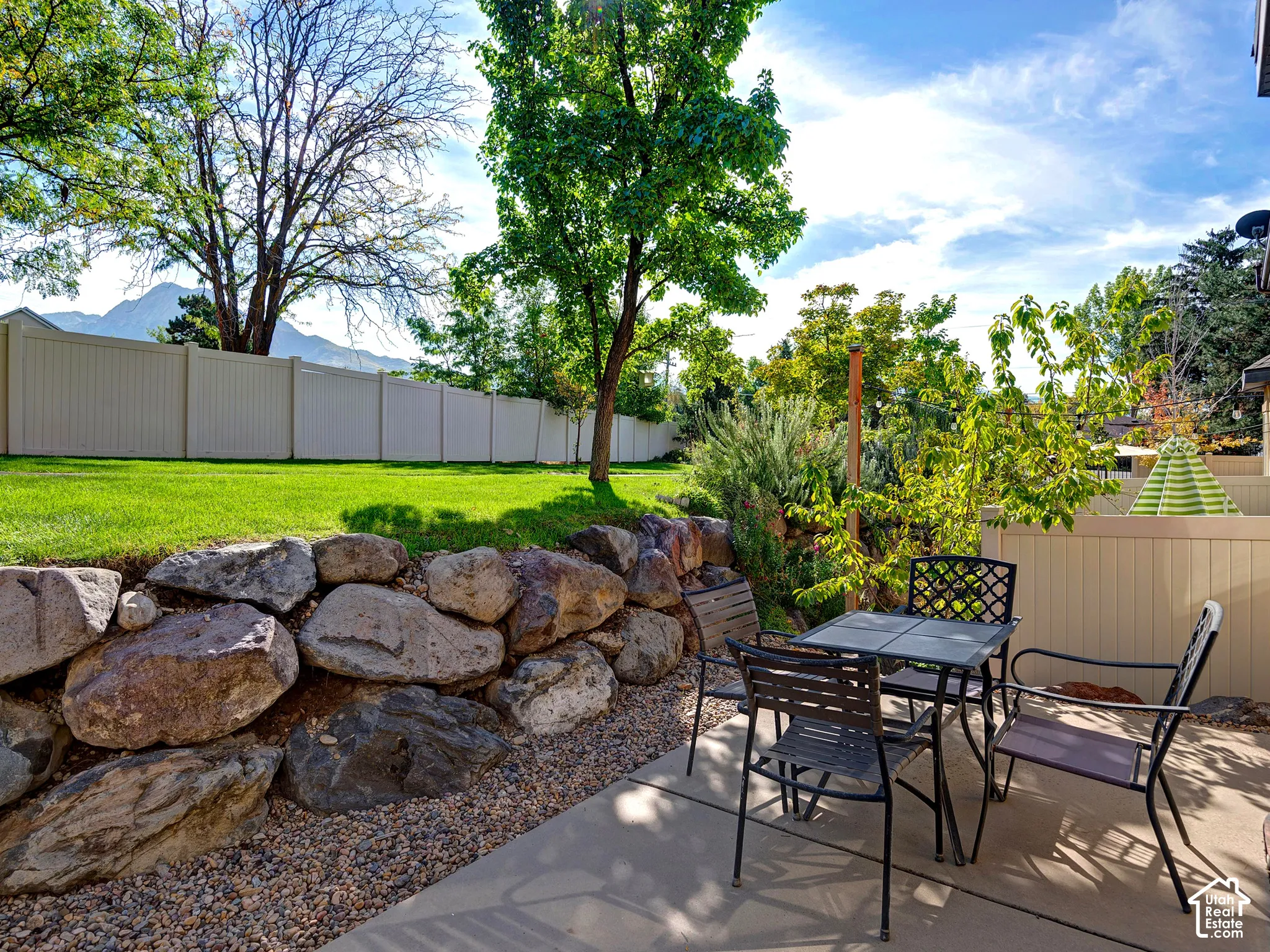 Paved patio area, stone retaining wall, gravel landscaping, green lawn, and privacy fencing