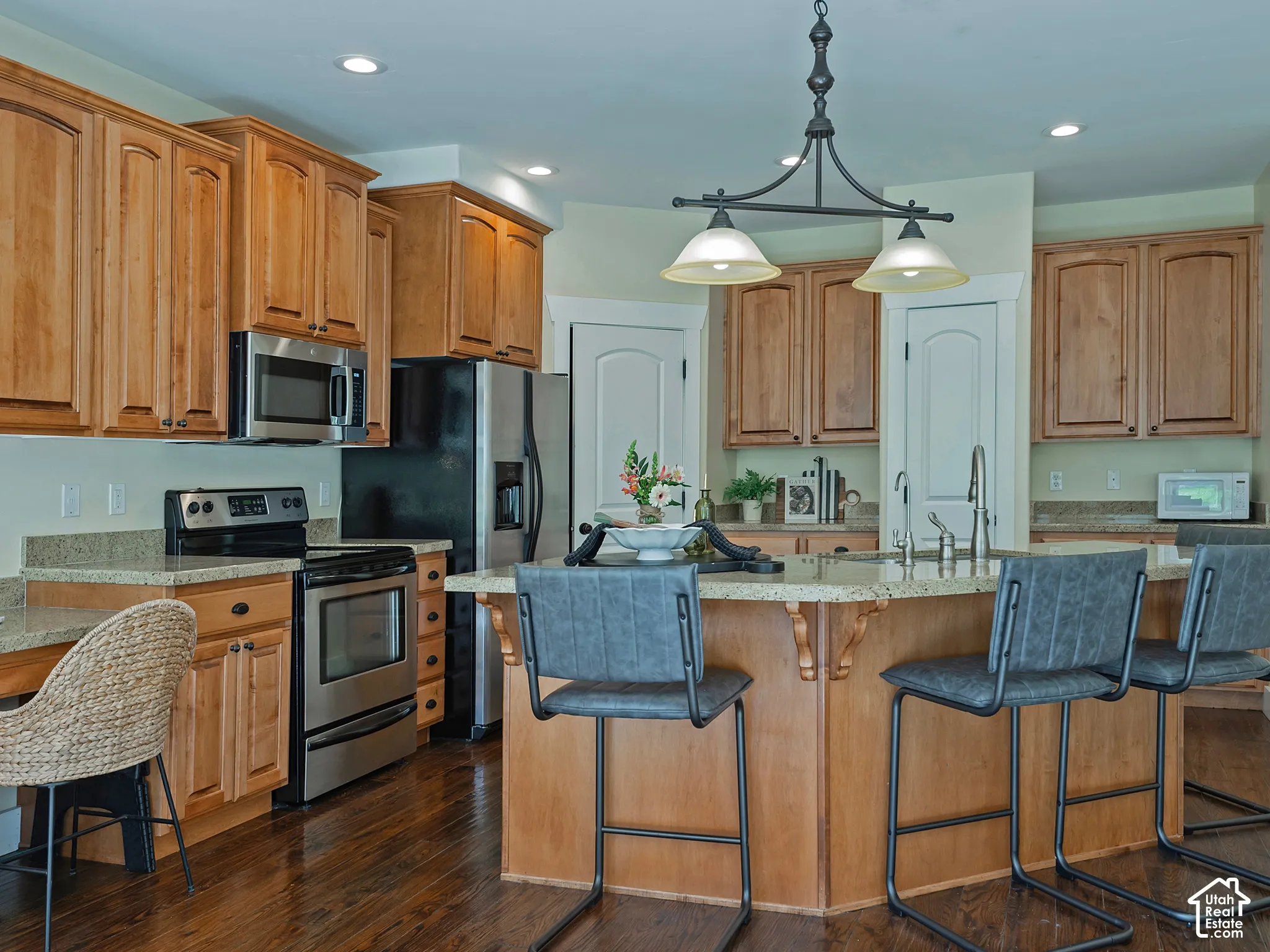Kitchen featuring wood-finish cabinetry, stainless steel appliances, granite countertops, a large island with seating, and dark wood-finish flooring