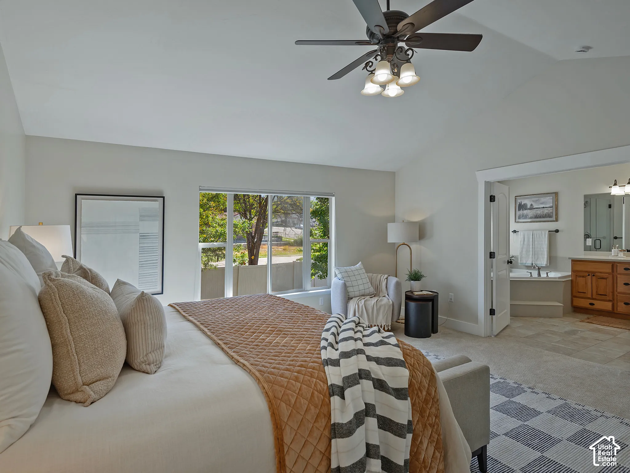 Vaulted ceiling with a ceiling fan light fixture, large window with natural light, attached three-panel door, built-in soaking tub, and a vanity with a double mirror