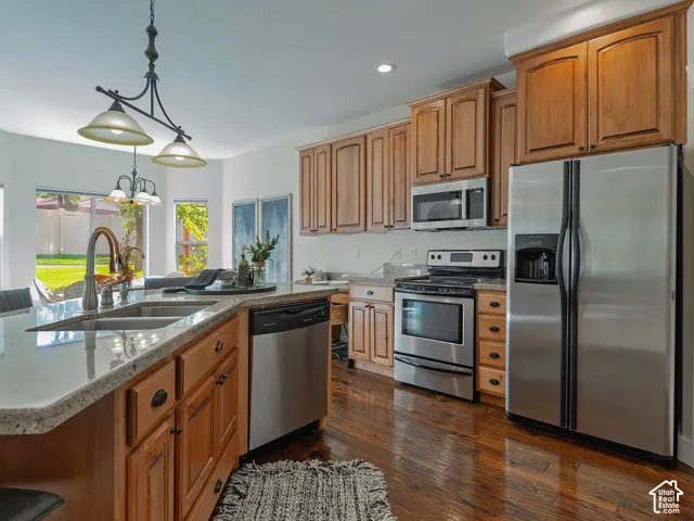 Kitchen featuring wood-finish cabinetry, stainless steel appliances, a center island with a double basin sink, and light-toned countertops